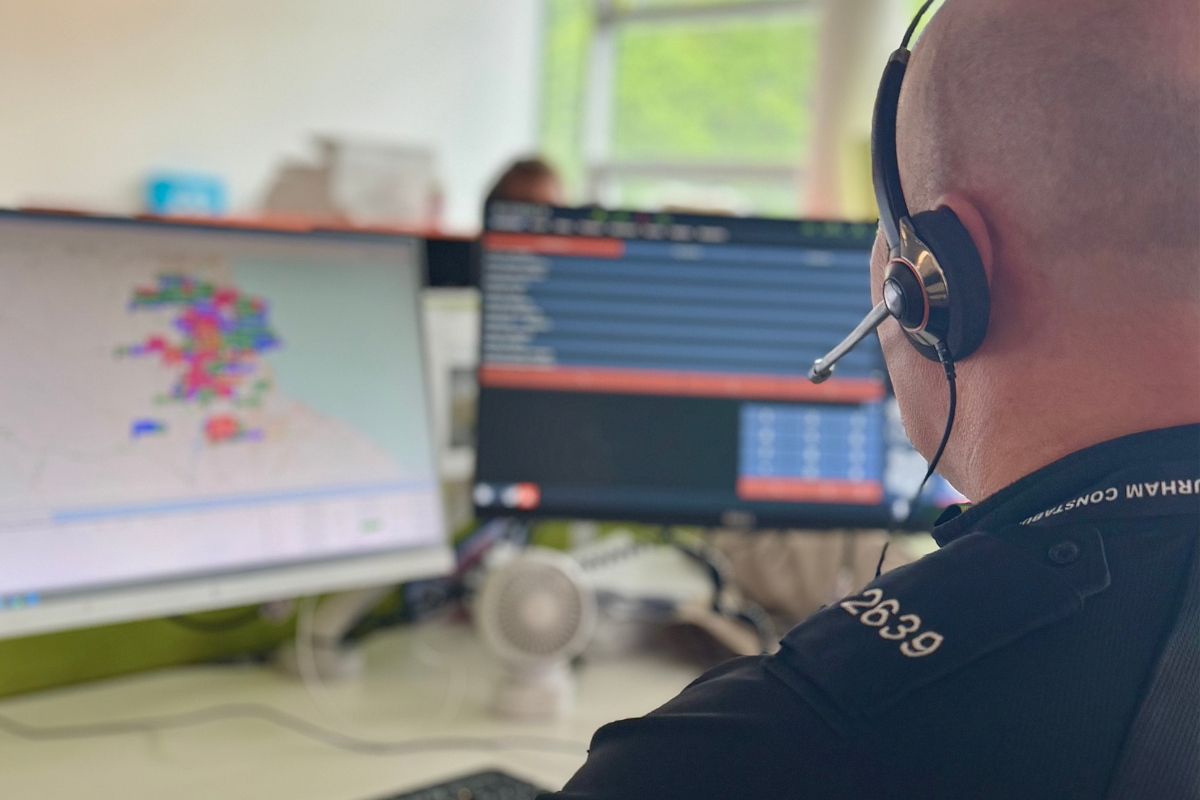 A call handler wearing a headset with his back to the camera facing his computer screen