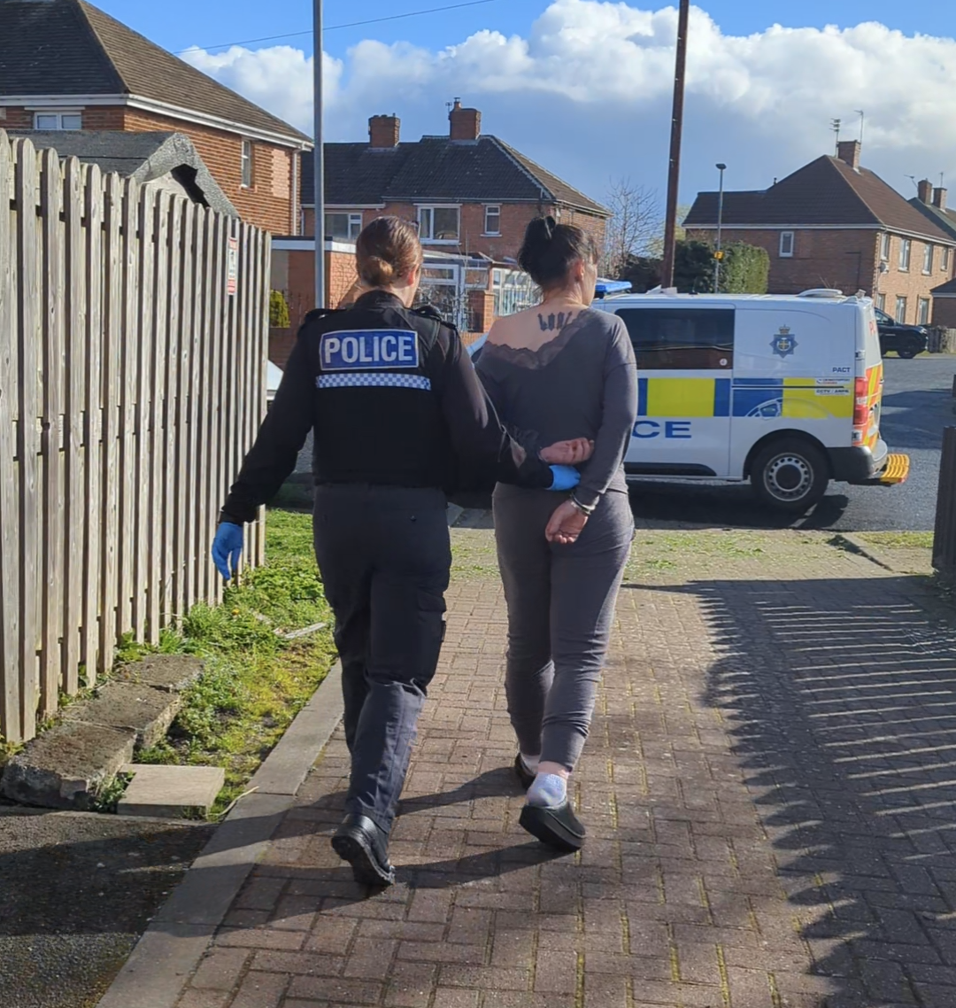 An officer walking the arrested woman to the police van in handcuffs