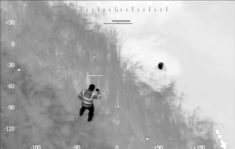 A black and white police helicopter image of the officer approaching the bog where the suspect is stuck