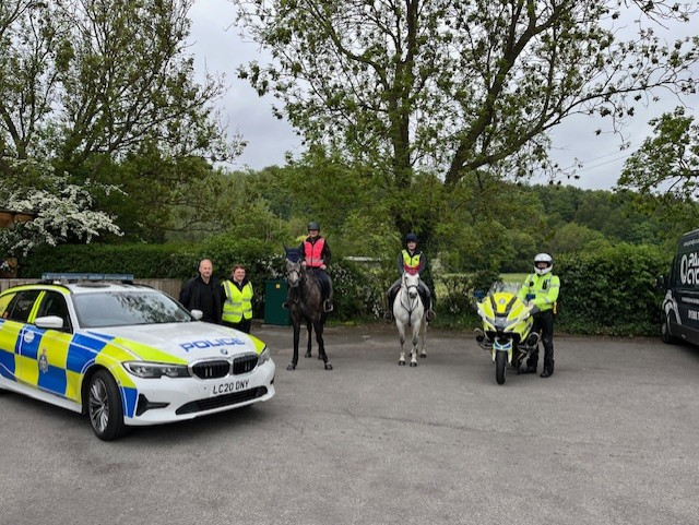 Two horseriders flanked by a police car and police motorbike